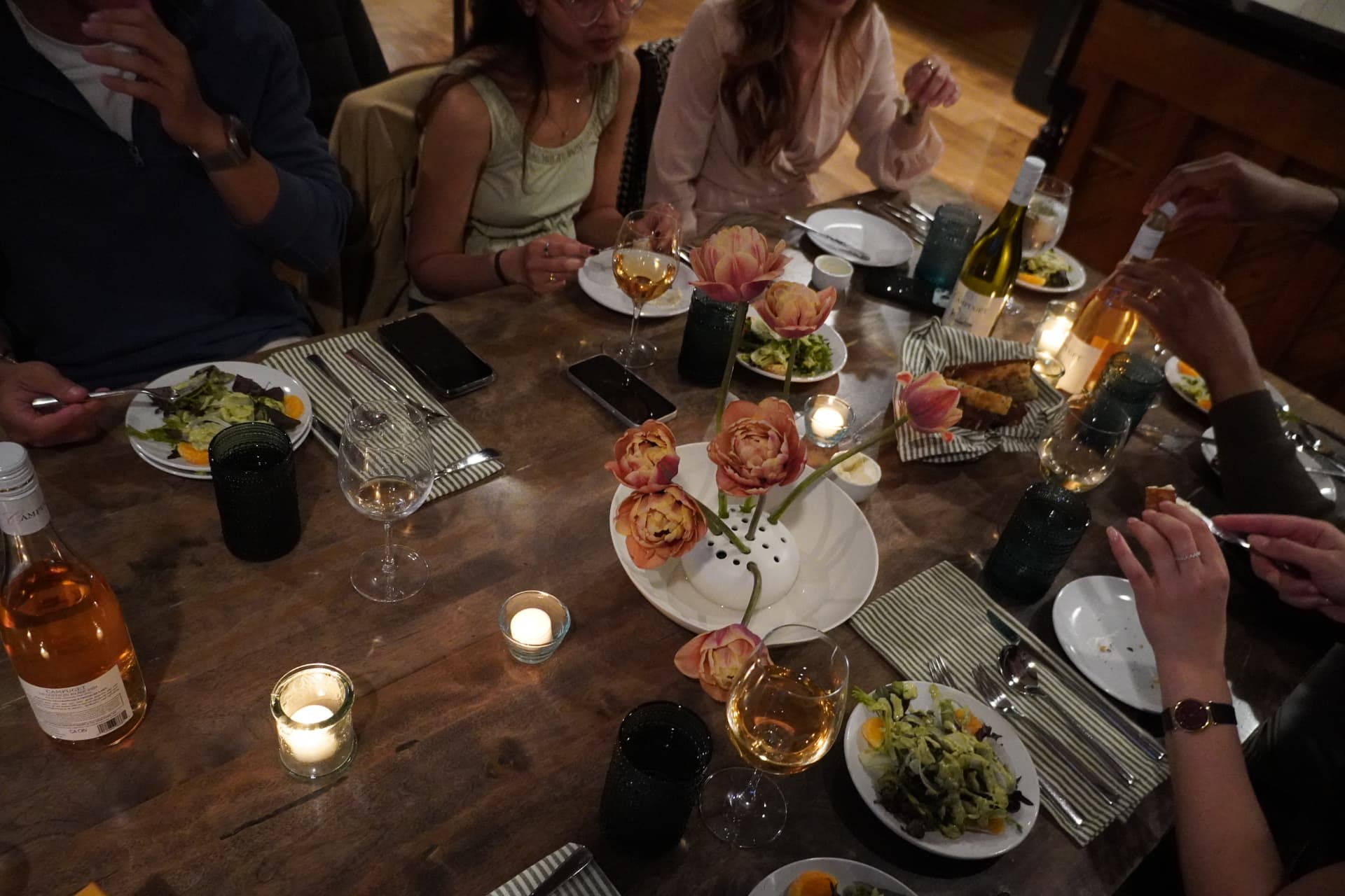 A long dinner table set with candles, wine, and tulips, mid-conversation