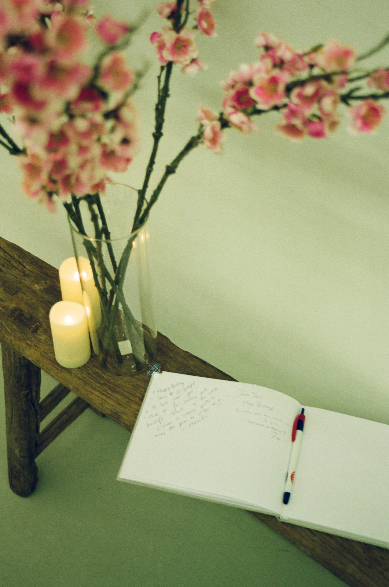 An open guest book beside candles and blossom branches on a wooden bench